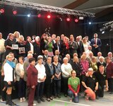 Eine Gruppe Menschen steht in zwei Reihen zusammen auf einer Bühne