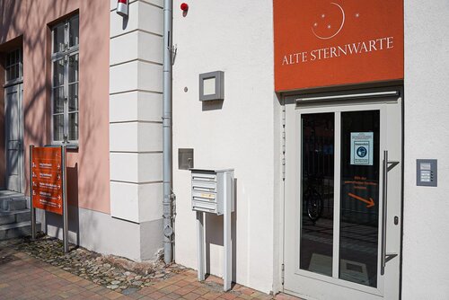 Ein Hauseingang neben einem Briefkasten und dem Gebäudenamen der Alten Sternwarte über dem Eingang