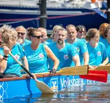 In einem großen Boot auf dem Wasser sitzen Menschen mit Paddeln und warten