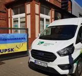 Ein Wagen des Pommerschen Diakonievereins steht neben einem Haus und einer ukrainischen Fahne