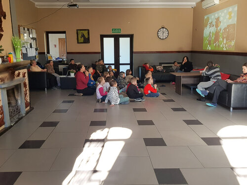 Eine Gruppe von Kindern sitzt auf einem großen Fliesenboden und schaut an der Wand auf einen projizierten Kinderfilm