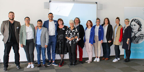 Eine Gruppe von Männern und Frauen stehen vor einem Flipchart