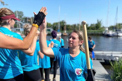Eine Frau mit einem Paddel geht an den Kolleginnen vorbei und klatscht in die Hand